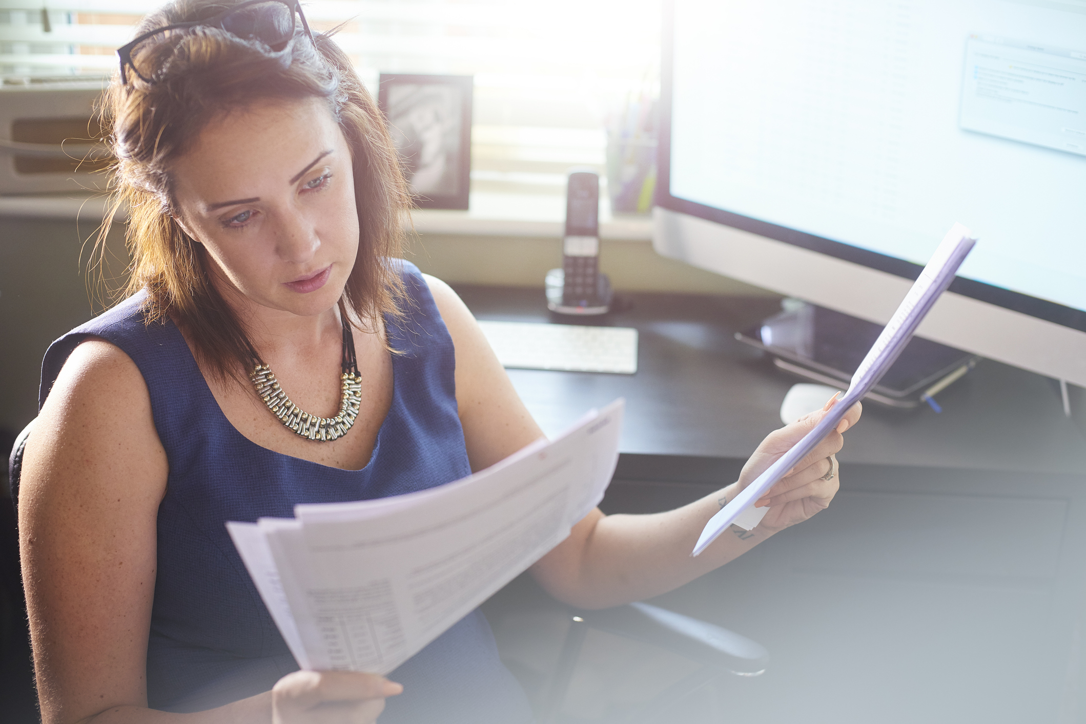 A businesswoman sits at her desk reading through paperwork