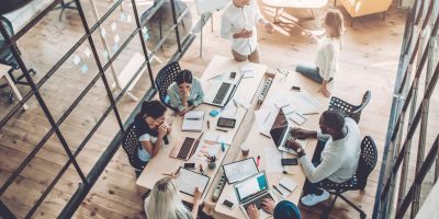 Top view of multiracial young creative people in modern office. Group of young business people are working together with laptop, tablet, smart phone, notebook. Successful hipster team in coworking. Freelancers.